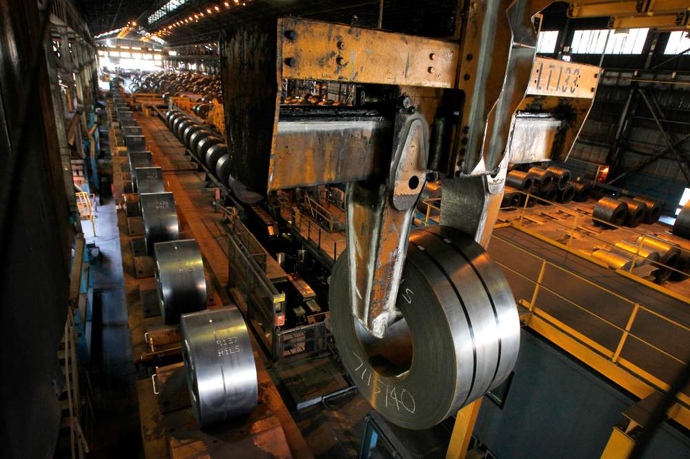 A crane moves a freshly-made steel coil through the processing area.