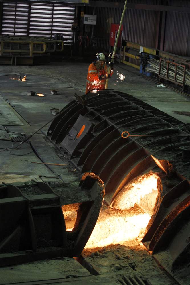 A worker in protective gear monitors the molten iron as it flows out of the blast furnace and into the trough.